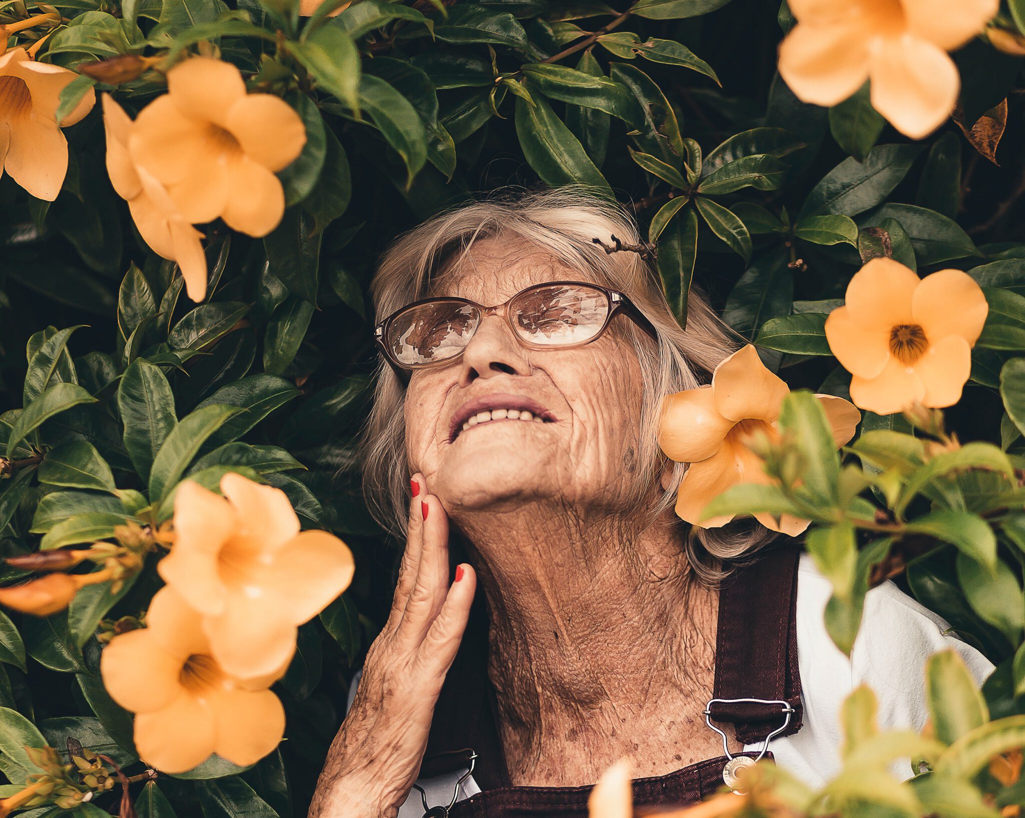 een oma met grijze haren voor een bosje met bloemen