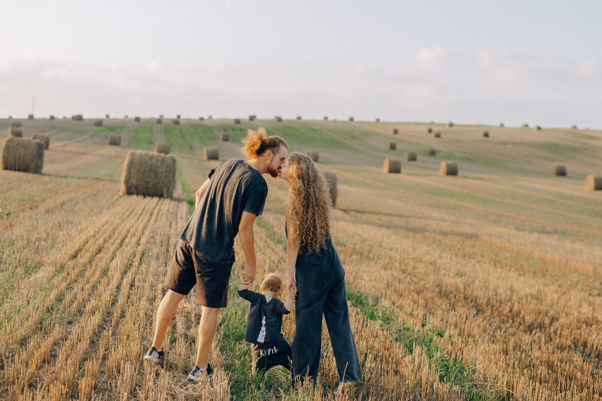 Man en vrouw met klein kindje kussen in veld met hooibalen