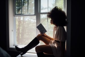 Vrouw die met een boek voor het raam zit te lezen