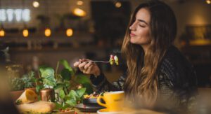 Vrouw zit met een vork te eten aan tafel