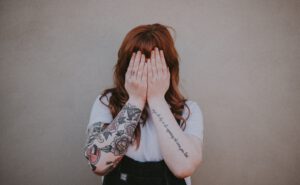 vrouw met tattoos en handen voor haar gezicht